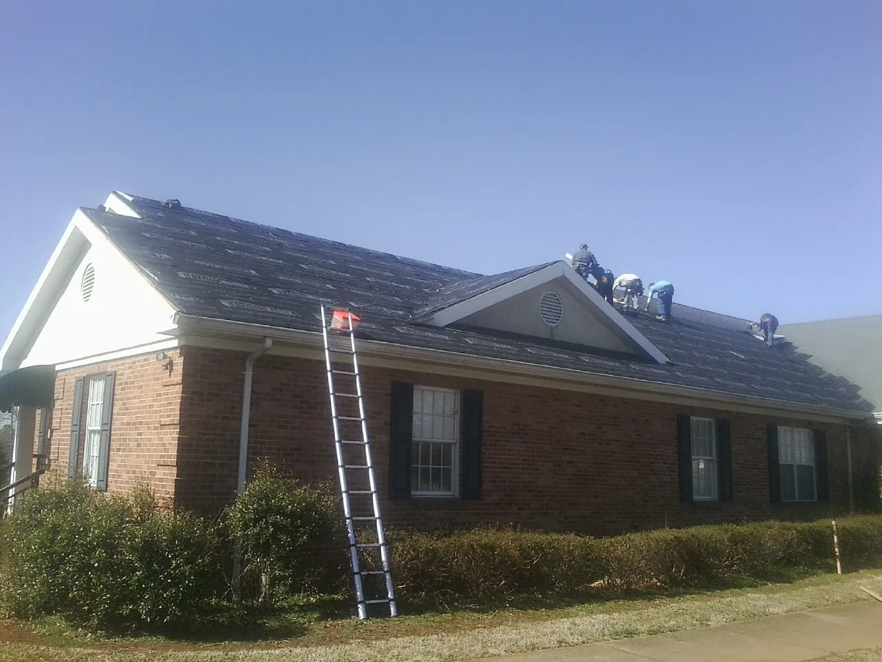 Crew tearing shingles off a brick ranch roof with a ladder set — Emergency Roof Repair work by our crew in Fallentimber