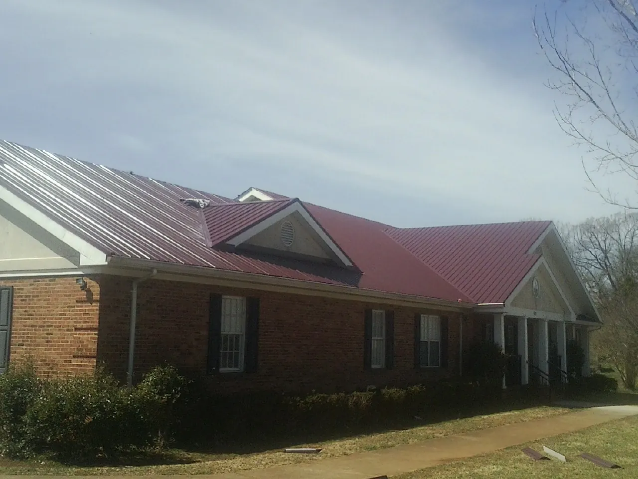 Red metal roof with gabled entries on a long brick building, from a Hail Damage Roof Repair job in Fallentimber