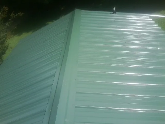 New green metal panels meeting at the ridge of a roof — Flat Roof Repair work by our crew in Fallentimber