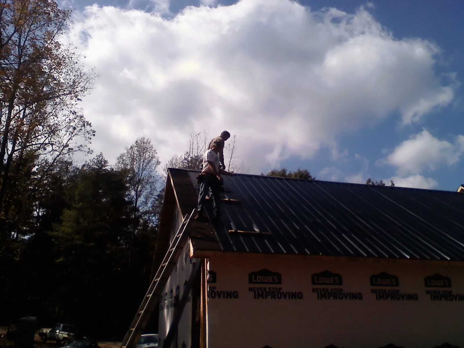 Roofer fastening dark metal panels high against a cloudy sky, from a Roof Inspection job in Fallentimber