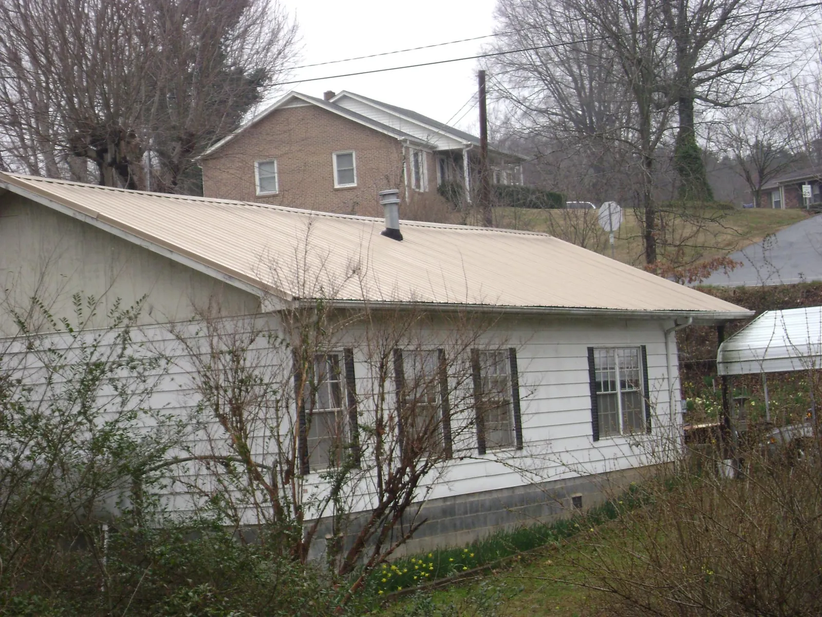 Tan metal roof on a white sided house set into a hillside — Commercial Roofing by Roofing Brothers in Fallentimber